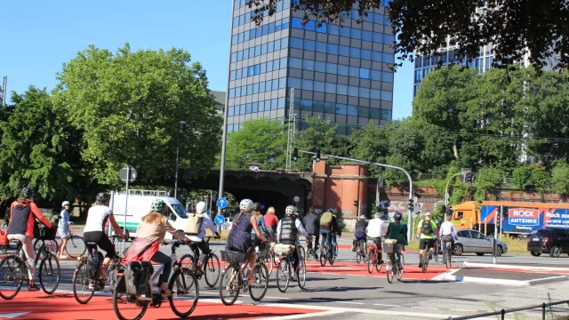 Knotenpunkt an der Alster mit sehr breiten, rot eingefärbten Radfahrstreifen und vielen Radfahrenden. © BVM Alster-Doppelknoten mit sehr breiten, rot markierten Radfahrstreifen; zahlreiche Radfahrende unterwegs.